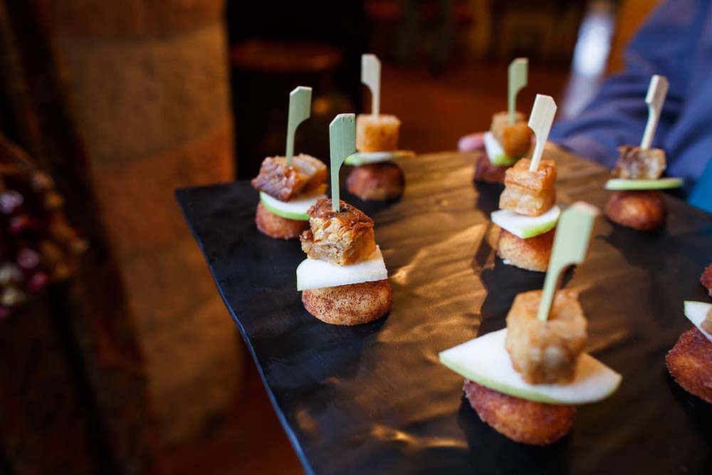 Footers Catering’s Sugar Donut Pork Belly Bite features White Marble Farms pork belly atop a slice of green apple and a cinnamon sugar donut hole, with black pepper syrup. Photo by Elevate Photography