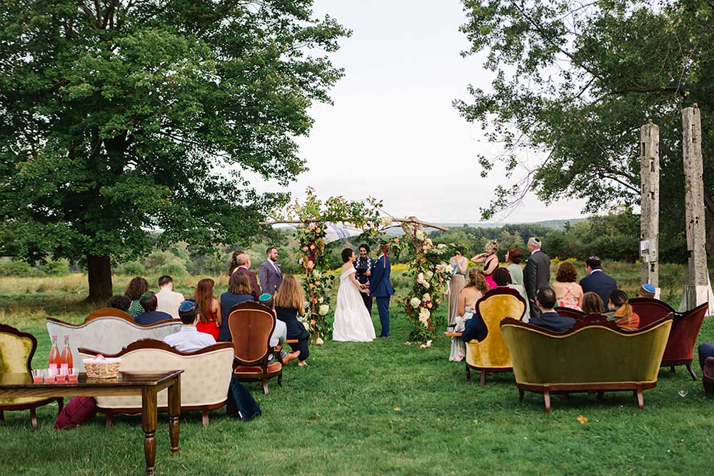 At a wedding designed by Social Maven, guests watch the outdoor ceremony from plush chairs and couches. Photo by Shaw Photography Co.