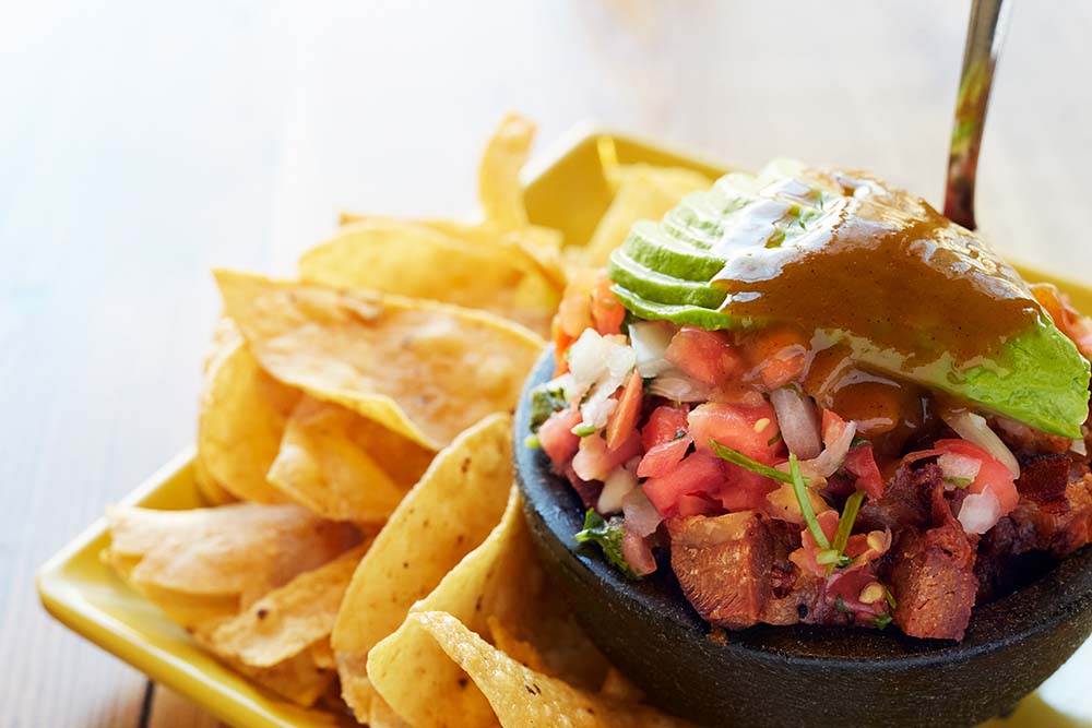 A popular appetizer at Irazú, chifrijo features fried pork, black beans, white rice, pico de gallo, avocado and salsa lizano.